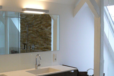 Mittelgroßes Nordisches Badezimmer En Suite mit flächenbündigen Schrankfronten, dunklen Holzschränken, Einbaubadewanne, offener Dusche, Wandtoilette, Steinplatten, weißer Wandfarbe, Keramikboden, integriertem Waschbecken, Mineralwerkstoff-Waschtisch und beigem Boden in Sonstige