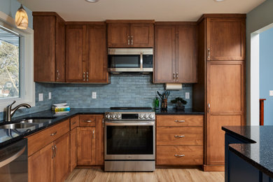 Eat-in kitchen - mid-sized transitional l-shaped vinyl floor and brown floor eat-in kitchen idea in Minneapolis with an undermount sink, shaker cabinets, medium tone wood cabinets, granite countertops, blue backsplash, porcelain backsplash, stainless steel appliances, an island and black countertops