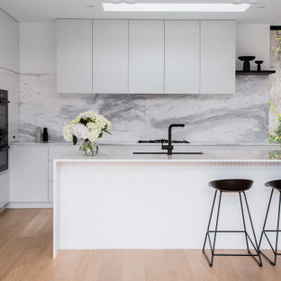Offene, Zweizeilige, Mittelgroße Moderne Küche mit Unterbauwaschbecken, flächenbündigen Schrankfronten, weißen Schränken, Mineralwerkstoff-Arbeitsplatte, Küchenrückwand in Grau, Rückwand aus Marmor, schwarzen Elektrogeräten, Sperrholzboden, Kücheninsel, beigem Boden, weißer Arbeitsplatte und eingelassener Decke in Melbourne