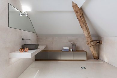 Großes Modernes Badezimmer En Suite in Dachschräge mit flächenbündigen Schrankfronten, grauen Schränken, Aufsatzwaschbecken, Wandtoilette mit Spülkasten, beigen Fliesen, Kalkfliesen, weißer Wandfarbe, Kalkstein, beigem Boden und beiger Waschtischplatte in Sonstige