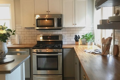 Example of a large transitional l-shaped ceramic tile enclosed kitchen design in Cleveland with a farmhouse sink, shaker cabinets, gray cabinets, wood countertops, white backsplash, subway tile backsplash, stainless steel appliances and an island
