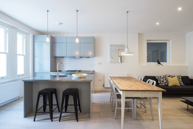 Photo of a contemporary galley open plan kitchen in London with flat-panel cabinets, grey cabinets, stainless steel benchtops, white splashback, subway tile splashback, panelled appliances, light hardwood floors and with island.