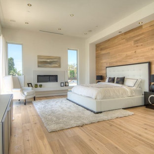 Geräumiges Modernes Hauptschlafzimmer mit weißer Wandfarbe, hellem Holzboden, Gaskamin, Kaminumrandung aus Beton und braunem Boden in Los Angeles