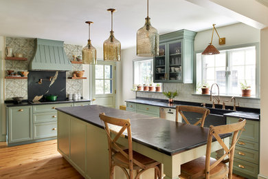 Mid-sized french country u-shaped medium tone wood floor and brown floor eat-in kitchen photo in Philadelphia with a farmhouse sink, shaker cabinets, green cabinets, soapstone countertops, multicolored backsplash, ceramic backsplash, stainless steel appliances, an island and black countertops