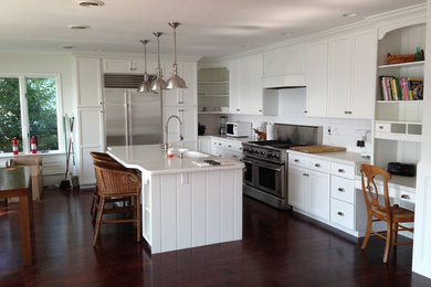 Example of a mid-sized island style l-shaped dark wood floor and brown floor open concept kitchen design in New York with a double-bowl sink, recessed-panel cabinets, white cabinets, quartz countertops, white backsplash, subway tile backsplash, stainless steel appliances and an island