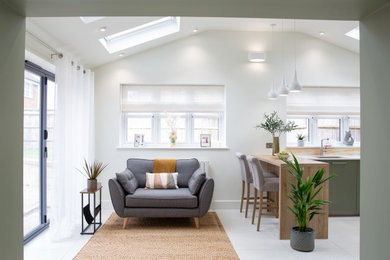 Large modern u-shaped open plan kitchen with a built-in sink, flat-panel cabinets, green cabinets, quartz worktops, orange splashback, glass sheet splashback, integrated appliances, porcelain flooring, a breakfast bar, beige floors, white worktops, a vaulted ceiling and feature lighting.
