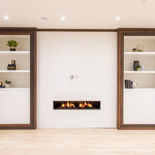 Photo of a medium sized contemporary look-out basement in Toronto with grey walls, light hardwood flooring, a ribbon fireplace, a plastered fireplace surround and brown floors.