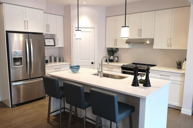 Example of a minimalist l-shaped medium tone wood floor and brown floor open concept kitchen design in Other with an undermount sink, shaker cabinets, white cabinets, quartz countertops, stainless steel appliances, an island and white countertops