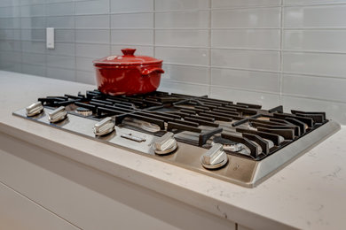 Inspiration for a large contemporary galley light wood floor and multicolored floor eat-in kitchen remodel in Calgary with an undermount sink, flat-panel cabinets, white cabinets, quartz countertops, gray backsplash, glass tile backsplash, stainless steel appliances, an island and white countertops