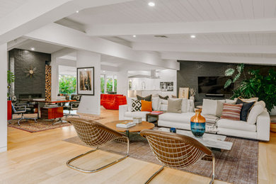 Photo of an expansive midcentury open concept living room in Los Angeles with multi-coloured walls, light hardwood floors, a ribbon fireplace, a brick fireplace surround and a wall-mounted tv.