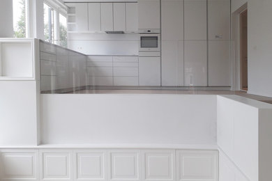 Photo of a large modern l-shaped open plan kitchen in Amsterdam with a double-bowl sink, white cabinets, solid surface benchtops, white splashback, white appliances, light hardwood floors, no island, brown floor and white benchtop.