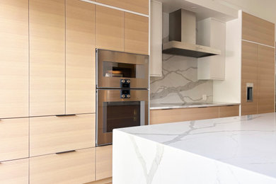 Open concept kitchen - large modern single-wall medium tone wood floor and vaulted ceiling open concept kitchen idea in Ottawa with flat-panel cabinets, light wood cabinets, quartz countertops, white backsplash, quartz backsplash, an island and white countertops