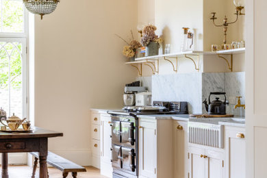 This is an example of a large traditional eat-in kitchen in Other with a farmhouse sink, shaker cabinets, beige cabinets, marble benchtops, white splashback, marble splashback, black appliances, medium hardwood floors, no island, brown floor and white benchtop.