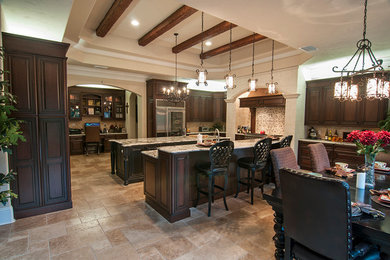 Eat-in kitchen - huge traditional l-shaped travertine floor eat-in kitchen idea in Orlando with an undermount sink, raised-panel cabinets, dark wood cabinets, granite countertops, beige backsplash, stone tile backsplash, stainless steel appliances and two islands