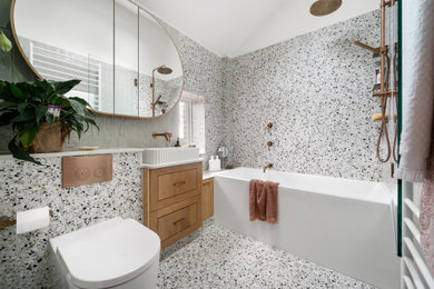 Inspiration for a small contemporary master bathroom in Melbourne with shaker cabinets, medium wood cabinets, a drop-in tub, a shower/bathtub combo, a one-piece toilet, multi-coloured tile, porcelain tile, multi-coloured walls, terrazzo floors, a vessel sink, engineered quartz benchtops, multi-coloured floor, a hinged shower door, white benchtops, a single vanity, a built-in vanity, vaulted and planked wall panelling.