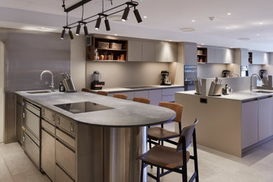Photo of an expansive contemporary grey and brown galley open plan kitchen in Berkshire with a single-bowl sink, flat-panel cabinets, beige cabinets, concrete worktops, grey splashback, engineered quartz splashback, black appliances, porcelain flooring, multiple islands, beige floors and grey worktops.