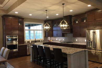Inspiration for a large transitional l-shaped medium tone wood floor eat-in kitchen remodel in Other with medium tone wood cabinets, granite countertops, stainless steel appliances, an island, a farmhouse sink and shaker cabinets