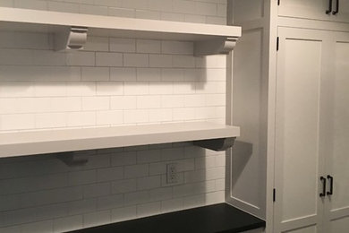Dedicated laundry room - mid-sized transitional single-wall slate floor dedicated laundry room idea in New York with recessed-panel cabinets, white cabinets, white walls and a stacked washer/dryer