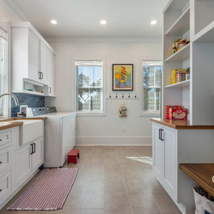 Immagine di una lavanderia stile marino con lavello stile country, ante in stile shaker, ante bianche, top in legno, paraspruzzi blu, paraspruzzi in gres porcellanato, pareti bianche, pavimento in gres porcellanato, lavatrice e asciugatrice affiancate, pavimento grigio e top marrone