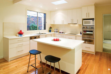 Design ideas for a mid-sized traditional l-shaped eat-in kitchen in Melbourne with a double-bowl sink, shaker cabinets, white cabinets, laminate benchtops, white splashback, ceramic splashback, stainless steel appliances, light hardwood floors and with island.