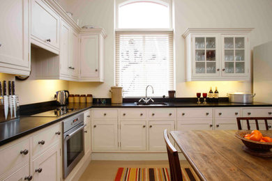 Inspiration for a small timeless l-shaped linoleum floor and beige floor enclosed kitchen remodel in London with an integrated sink, shaker cabinets, white cabinets, granite countertops, black backsplash, granite backsplash, stainless steel appliances, no island and black countertops