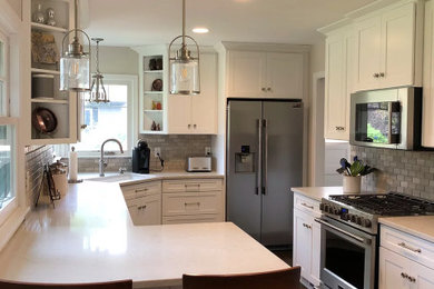 Example of a transitional u-shaped dark wood floor and brown floor eat-in kitchen design in Other with a drop-in sink, shaker cabinets, white cabinets, quartz countertops, gray backsplash, stone tile backsplash, stainless steel appliances, no island and white countertops