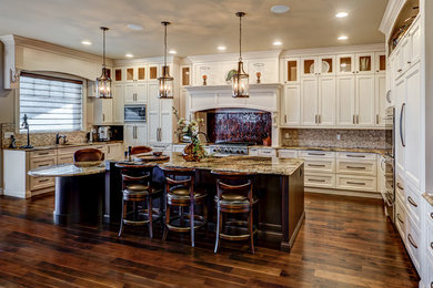 Example of a large classic u-shaped dark wood floor eat-in kitchen design in Edmonton with an undermount sink, recessed-panel cabinets, white cabinets, granite countertops, stone tile backsplash, paneled appliances and an island
