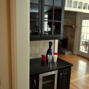 ボストンの小さいトランジショナルスタイルのおしゃれなホームバー (レイズドパネル扉のキャビネット、黒いキャビネット、人工大理石カウンター、ベージュキッチンパネル、淡色無垢フローリング、トラバーチンの床) の写真