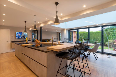 Design ideas for a large contemporary l-shaped open plan kitchen in Cheshire with a drop-in sink, flat-panel cabinets, medium wood cabinets, solid surface benchtops, black appliances, light hardwood floors, with island, beige floor and beige benchtop.