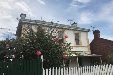 This is an example of a medium sized and white victorian bungalow detached house in Melbourne with stone cladding, a pitched roof and a tiled roof.
