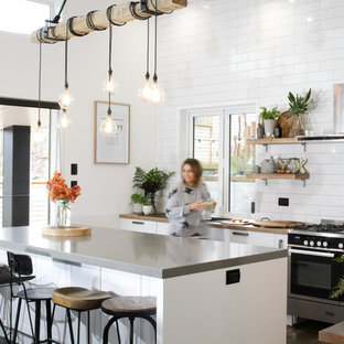 Zweizeilige, Mittelgroße Stilmix Küche mit Vorratsschrank, Landhausspüle, Schrankfronten im Shaker-Stil, weißen Schränken, Laminat-Arbeitsplatte, Küchenrückwand in Weiß, Rückwand aus Metrofliesen, Küchengeräten aus Edelstahl, Laminat, Kücheninsel und braunem Boden in Sonstige