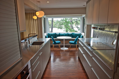 Example of a mid-sized minimalist galley medium tone wood floor open concept kitchen design in Other with a single-bowl sink, flat-panel cabinets, gray cabinets, stainless steel countertops, stone slab backsplash, stainless steel appliances, a peninsula and gray backsplash