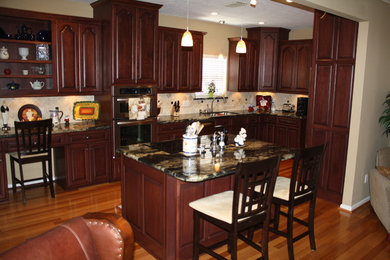 Open concept kitchen - mid-sized traditional l-shaped medium tone wood floor open concept kitchen idea in Houston with an undermount sink, raised-panel cabinets, dark wood cabinets, marble countertops, beige backsplash, stone tile backsplash, stainless steel appliances and an island