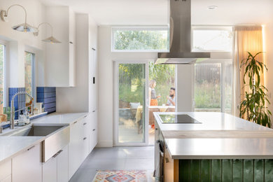 Example of a mid-sized galley ceramic tile and gray floor eat-in kitchen design in Seattle with a farmhouse sink, flat-panel cabinets, white cabinets, quartz countertops, blue backsplash, ceramic backsplash, stainless steel appliances, an island and white countertops