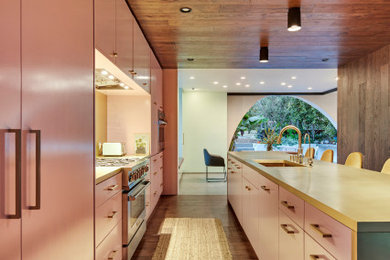 Large tuscan single-wall dark wood floor, wood ceiling and brown floor open concept kitchen photo in Los Angeles with an undermount sink, flat-panel cabinets, pink cabinets, yellow backsplash, metal backsplash, stainless steel appliances, an island and yellow countertops