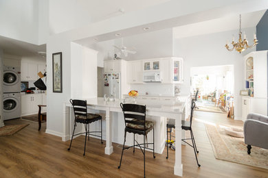 Example of a large transitional galley medium tone wood floor eat-in kitchen design in New York with recessed-panel cabinets, white cabinets, quartz countertops, a peninsula, an undermount sink and white appliances
