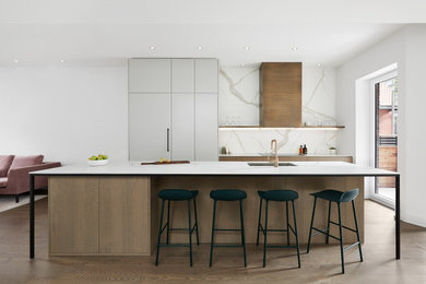 Example of a mid-sized minimalist single-wall medium tone wood floor open concept kitchen design in Montreal with an undermount sink, flat-panel cabinets, quartz countertops, white backsplash, paneled appliances, an island, white countertops and gray cabinets