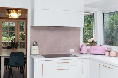 Inspiration for a mid-sized modern u-shaped open plan kitchen in Auckland with an undermount sink, flat-panel cabinets, white cabinets, solid surface benchtops, pink splashback, ceramic splashback, ceramic floors, no island and white benchtop.