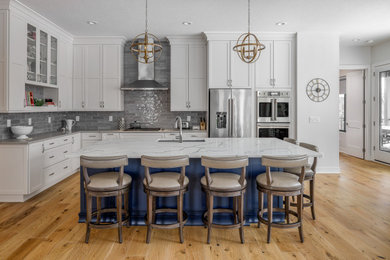 Inspiration for a transitional medium tone wood floor and brown floor kitchen remodel in Other with an undermount sink, shaker cabinets, white cabinets, gray backsplash, stainless steel appliances, an island and white countertops