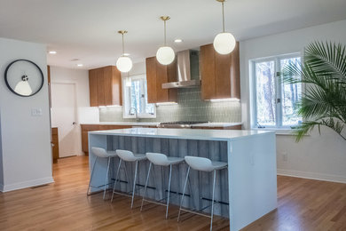 Large midcentury l-shaped open plan kitchen in Raleigh with an undermount sink, flat-panel cabinets, medium wood cabinets, quartz benchtops, green splashback, glass tile splashback, stainless steel appliances, medium hardwood floors and with island.