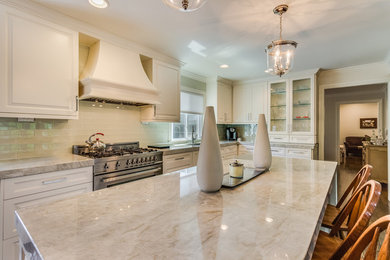 Example of a transitional medium tone wood floor and brown floor kitchen design in Detroit with a drop-in sink, raised-panel cabinets, white cabinets, marble countertops, glass tile backsplash, stainless steel appliances, an island and beige countertops
