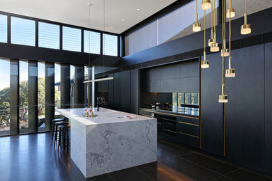Design ideas for a large contemporary galley open plan kitchen in Sydney with a double-bowl sink, flat-panel cabinets, black cabinets, mirror splashback, panelled appliances, with island, black floor and grey benchtop.