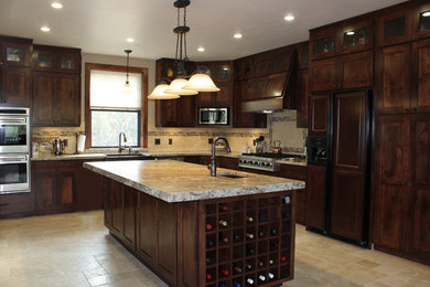 Inspiration for a large rustic l-shaped travertine floor and beige floor eat-in kitchen remodel in San Luis Obispo with a farmhouse sink, recessed-panel cabinets, dark wood cabinets, granite countertops, beige backsplash, stone tile backsplash, stainless steel appliances and an island