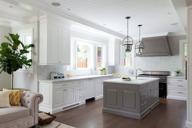 Traditional u-shaped open plan kitchen in San Francisco with white cabinets, marble benchtops, white splashback, black appliances, dark hardwood floors, with island and raised-panel cabinets.