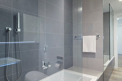 Bathroom - large contemporary master gray tile and porcelain tile medium tone wood floor and beige floor bathroom idea in New York with a one-piece toilet, flat-panel cabinets, white cabinets, white walls, an integrated sink and glass countertops