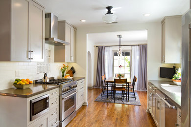 This is an example of a transitional galley eat-in kitchen in Los Angeles with an undermount sink, shaker cabinets, grey cabinets, white splashback, subway tile splashback, stainless steel appliances and medium hardwood floors.