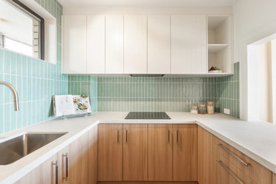 This is an example of a small modern u-shaped separate kitchen in Sydney with an undermount sink, flat-panel cabinets, light wood cabinets, green splashback, subway tile splashback, black appliances and beige benchtop.