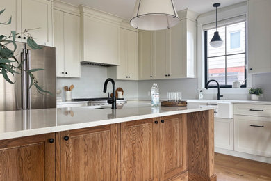 Inspiration for a transitional l-shaped medium tone wood floor kitchen remodel in Ottawa with a farmhouse sink, shaker cabinets, beige cabinets, quartz countertops, white backsplash, subway tile backsplash, stainless steel appliances, an island and white countertops