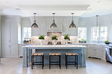 Photo of a large beach style l-shaped eat-in kitchen in Boston with an undermount sink, recessed-panel cabinets, white cabinets, marble benchtops, grey splashback, subway tile splashback, with island, stainless steel appliances and light hardwood floors.
