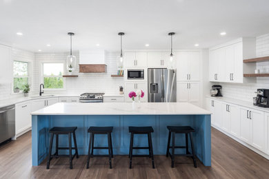 Inspiration for a large transitional u-shaped medium tone wood floor and brown floor eat-in kitchen remodel in Vancouver with an undermount sink, shaker cabinets, white cabinets, quartz countertops, white backsplash, ceramic backsplash, stainless steel appliances, an island and white countertops
